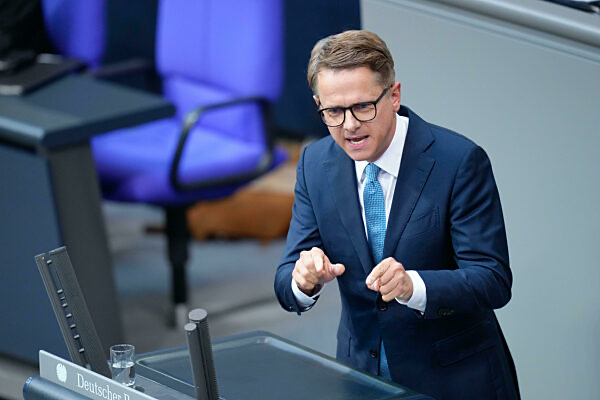 Carsten Linnemann speaking at the lectern of the German Bundestag, blue plenary chairs behind him
