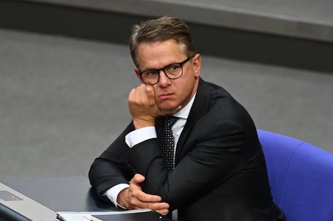 Carsten Linnemann seated in the Bundestag plenary, hand on chin, listening