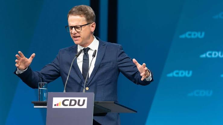 Carsten Linnemann speaking at a CDU lectern in front of a blue CDU backdrop