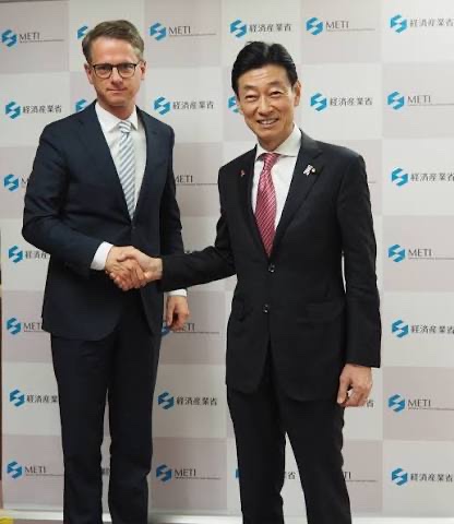 Carsten Linnemann shaking hands with a Japanese official in front of a backdrop of Japan's Ministry of Economy, Trade and Industry