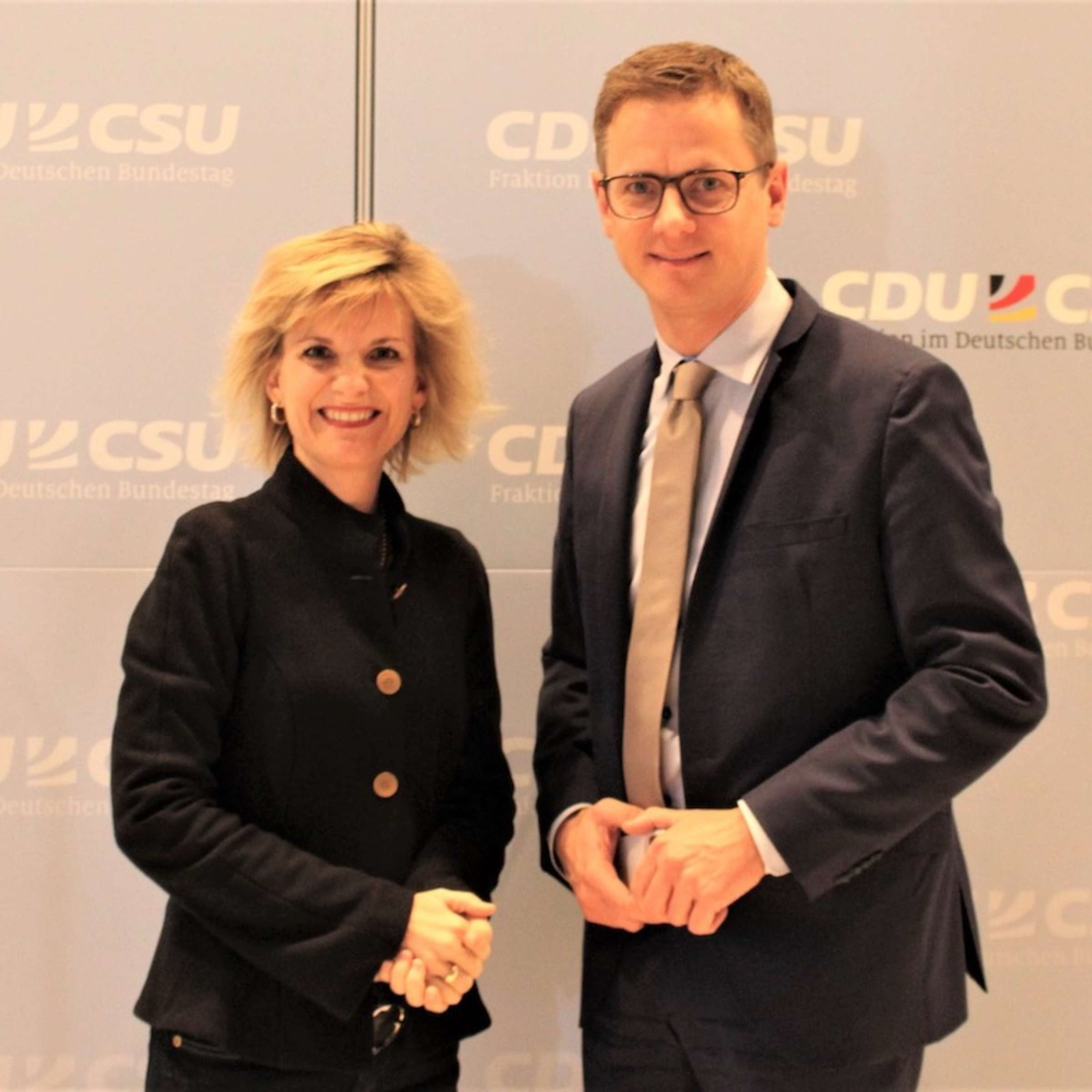 Carsten Linnemann standing beside a woman in front of a CDU/CSU parliamentary group backdrop
