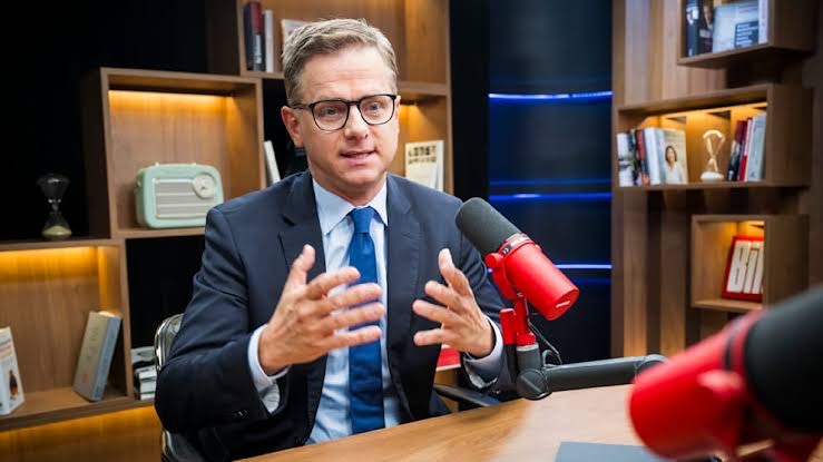 Carsten Linnemann speaking in an interview studio with a red microphone and bookshelves in the background