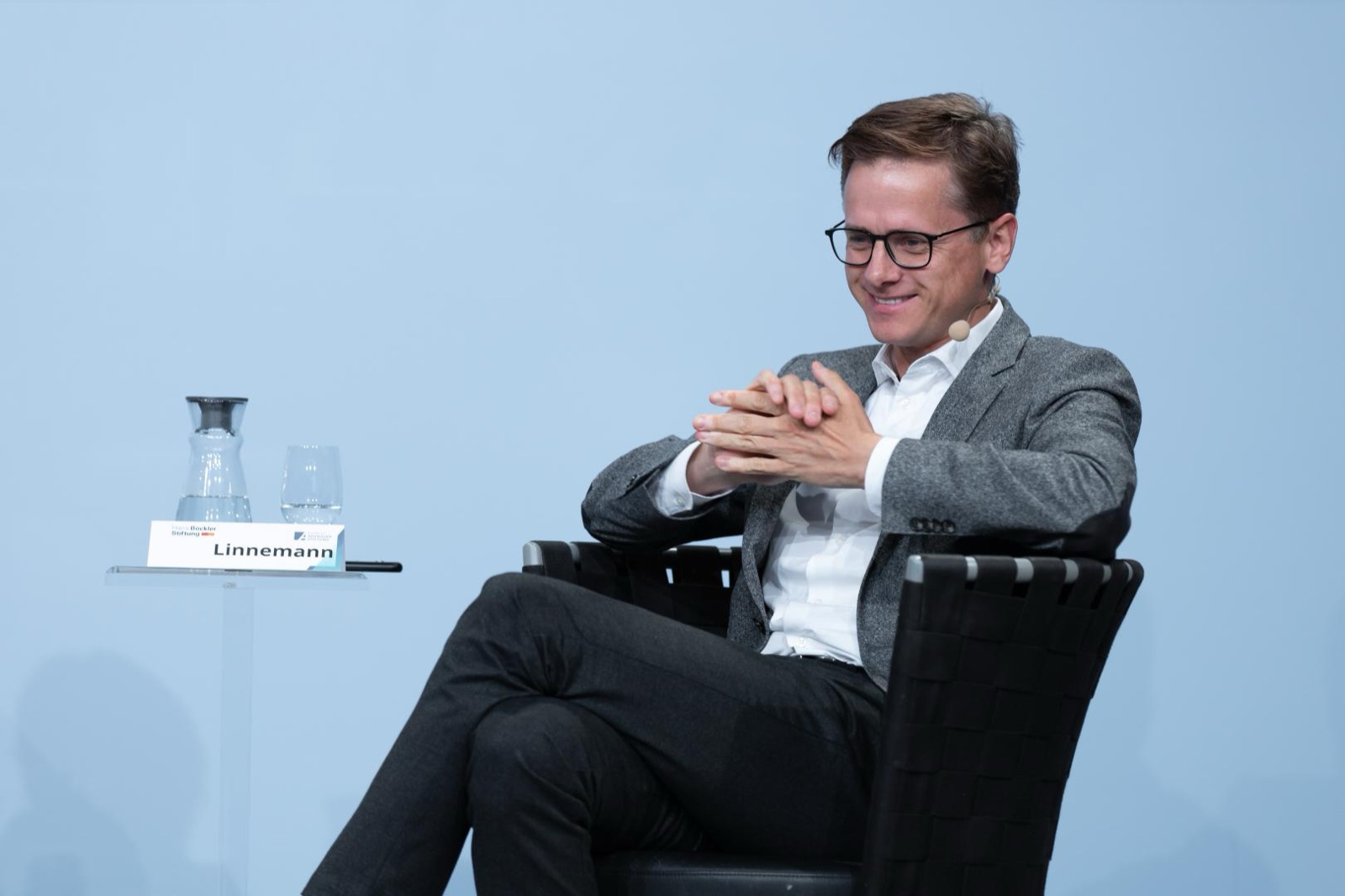 Carsten Linnemann seated on a panel stage behind a name card reading Linnemann, light-blue backdrop